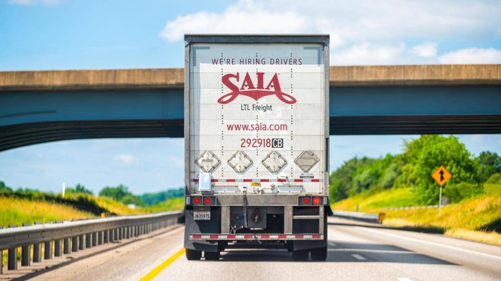 A semi truck is driving down a highway under a bridge.