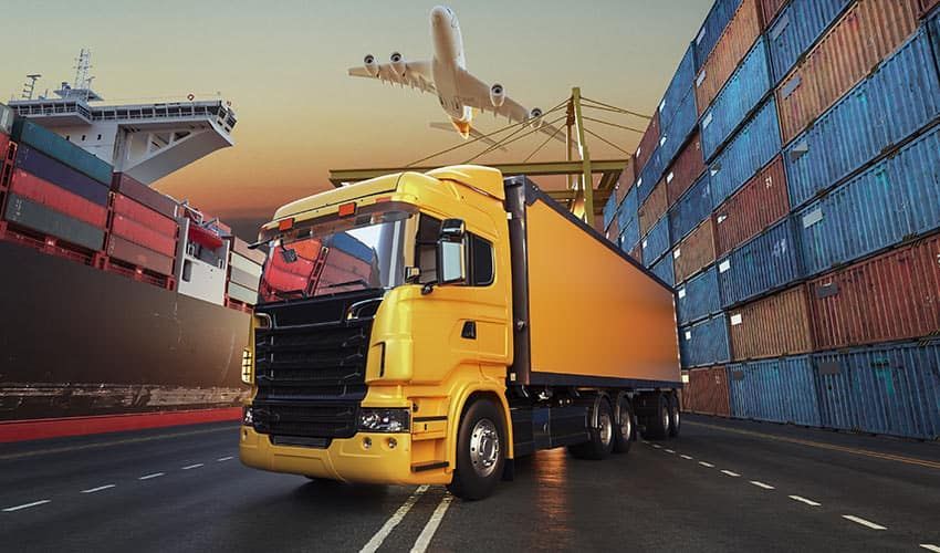 A yellow truck is driving down a road next to a container ship.