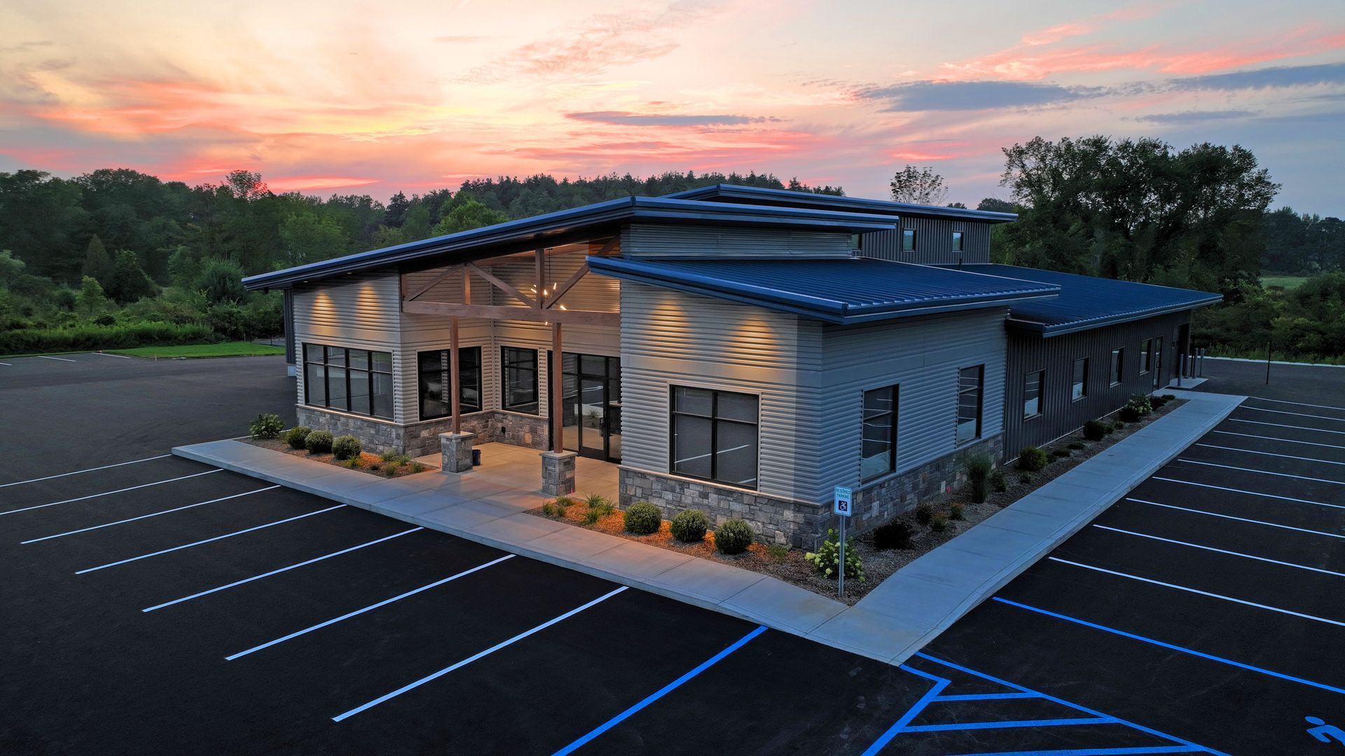 An aerial view of a large building with a parking lot in front of it at sunset.