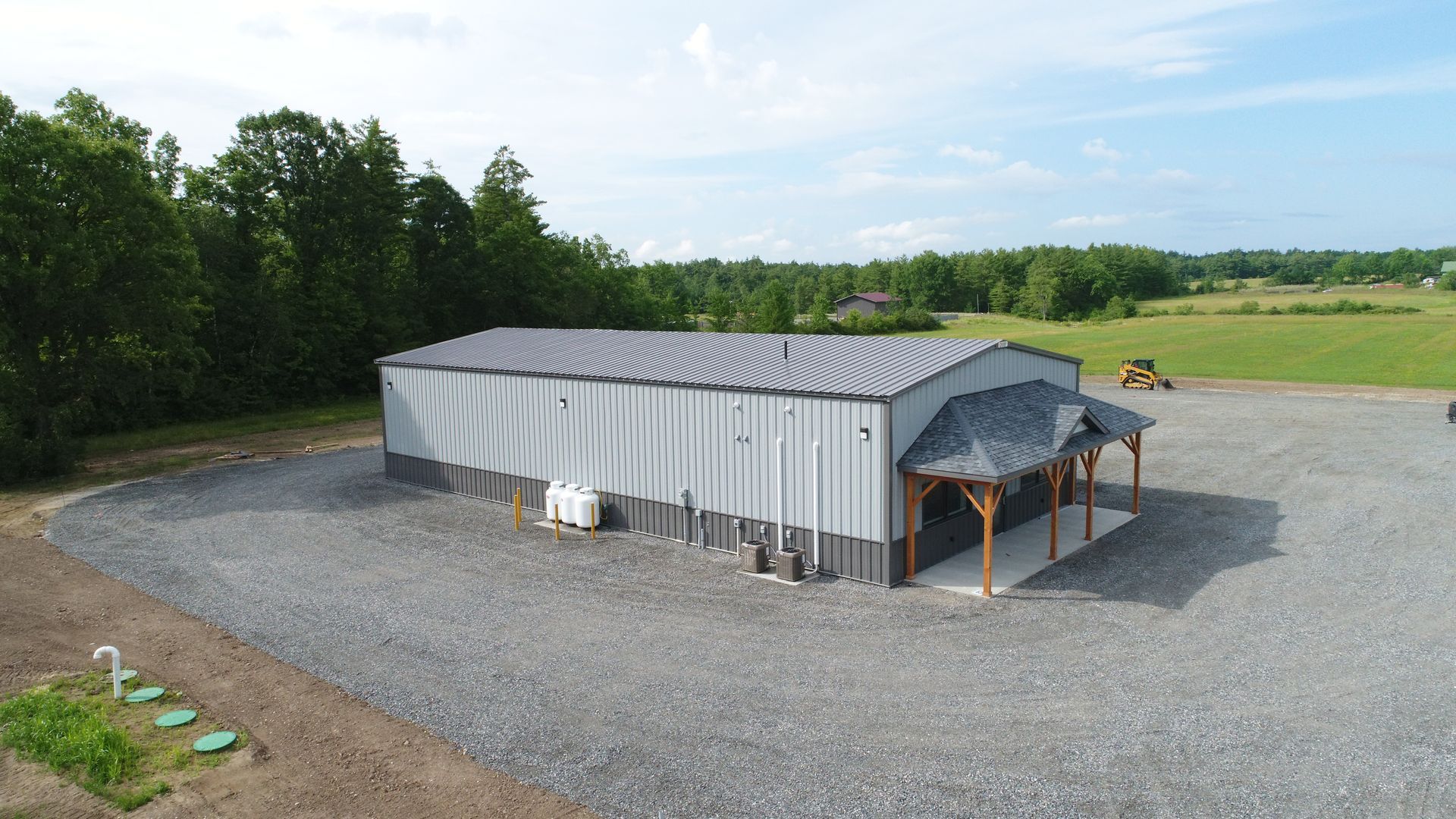 An aerial view of a large metal building with a porch and trees in the background.