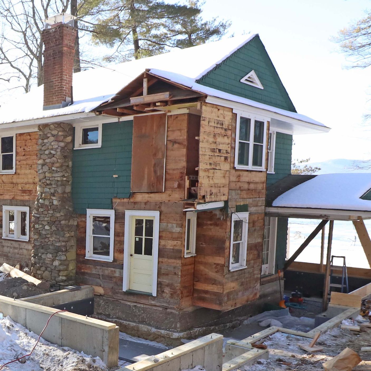 A wooden house with a green roof is being remodeled