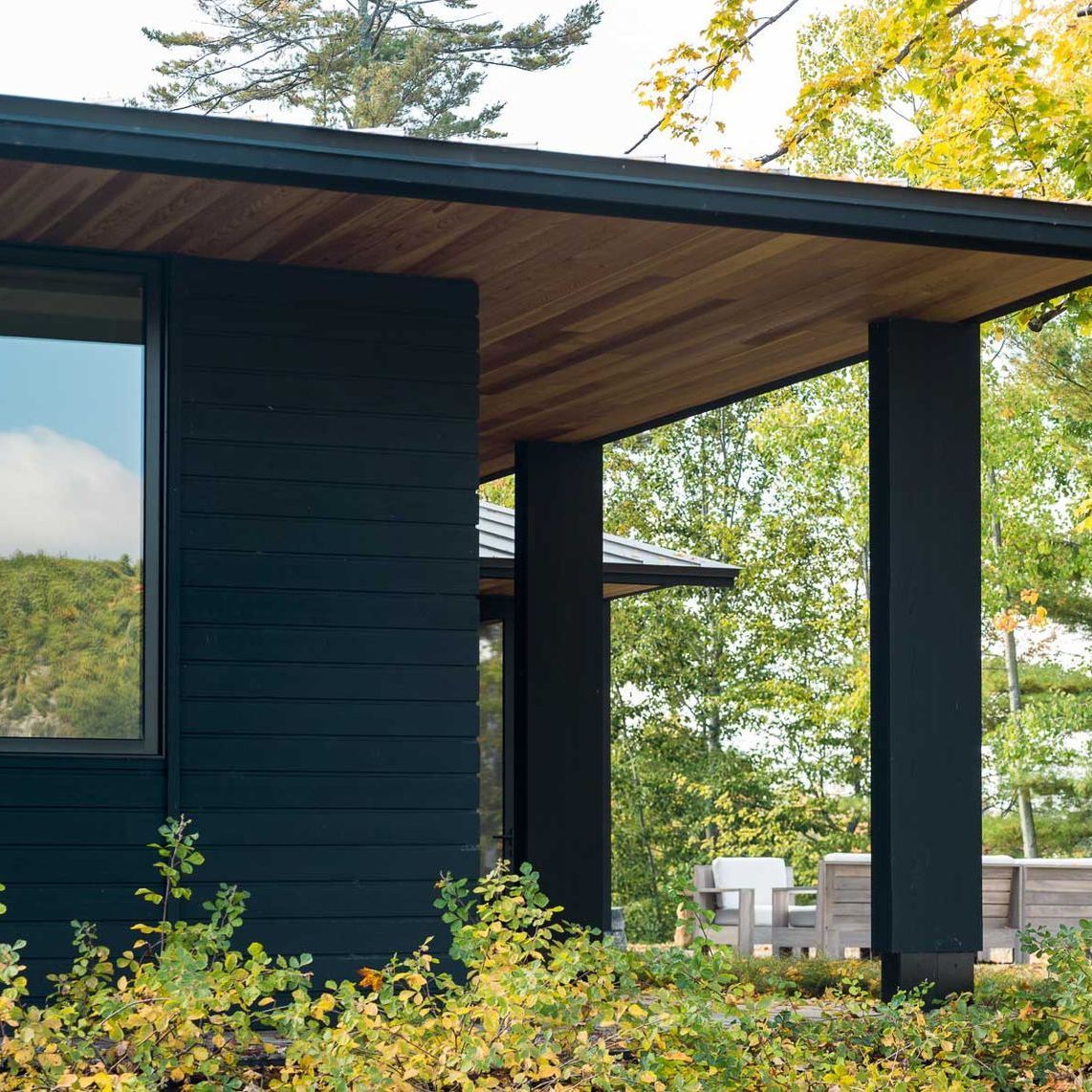 A black house with a wooden roof is surrounded by trees and bushes.