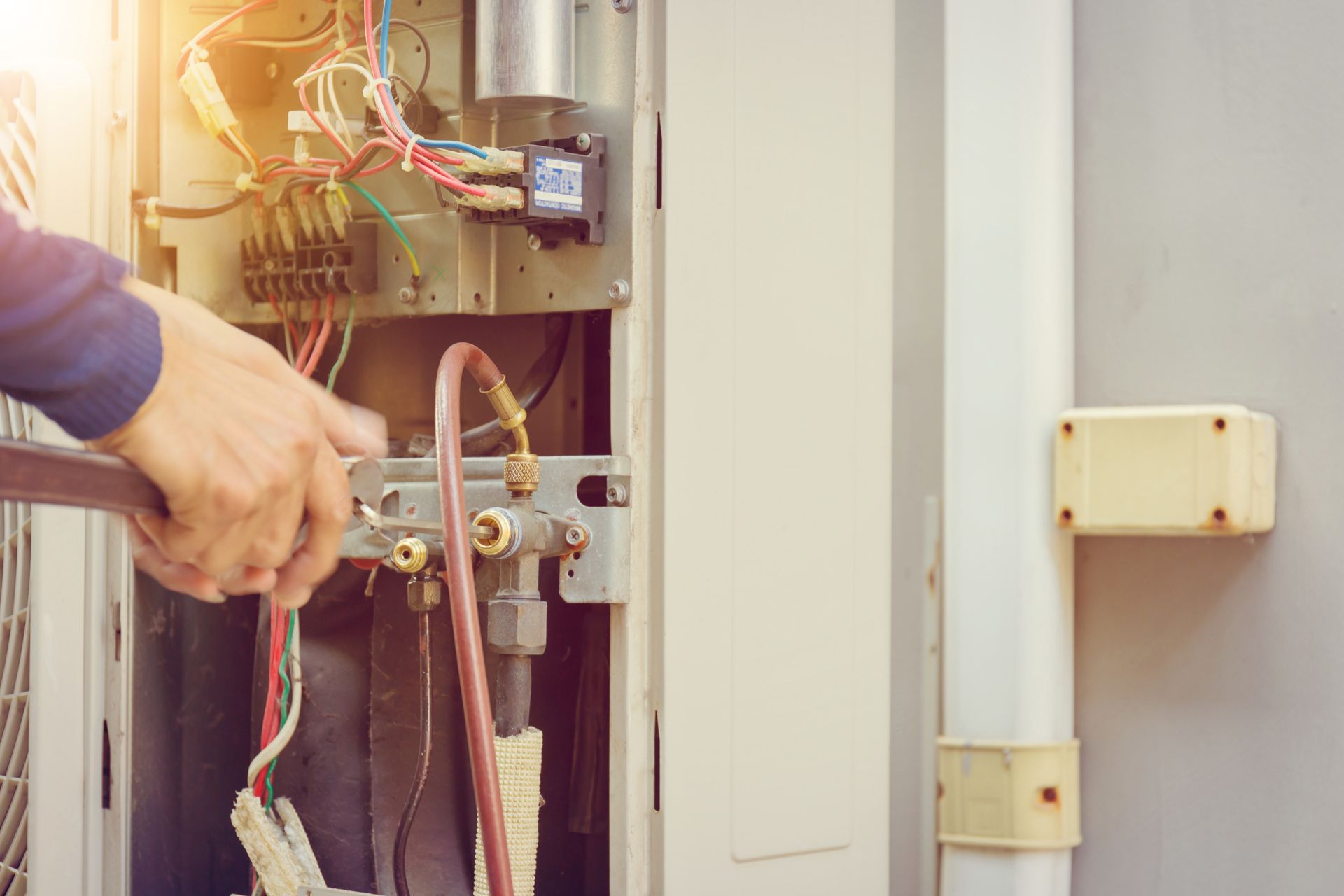 Person using a wrench to work on electrical components inside an HVAC unit.