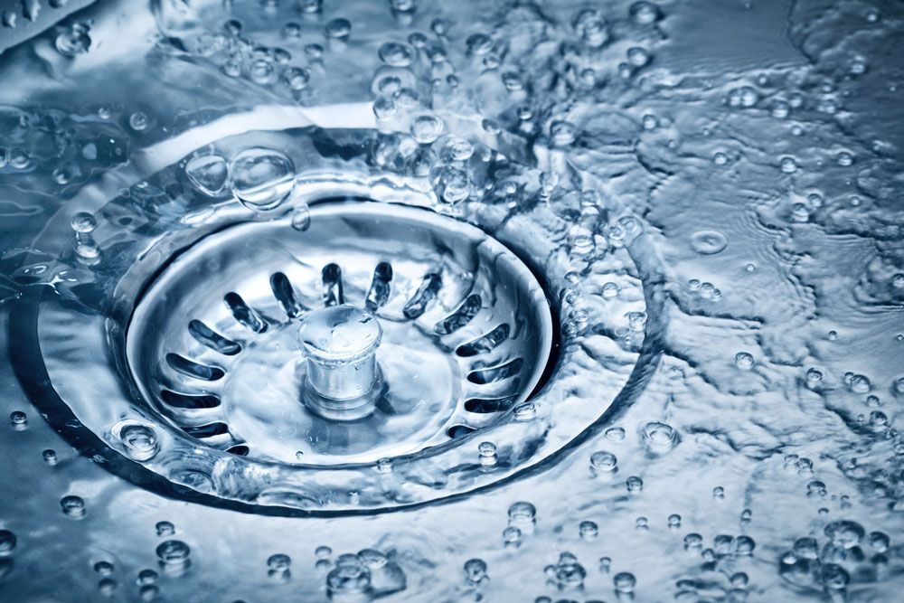 Water gushes down a shiny, metal sink drain, creating splashes and bubbles.