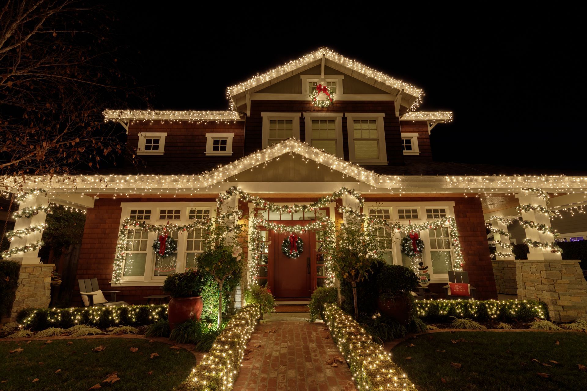 A house decorated with white Christmas lights and wreaths at night.