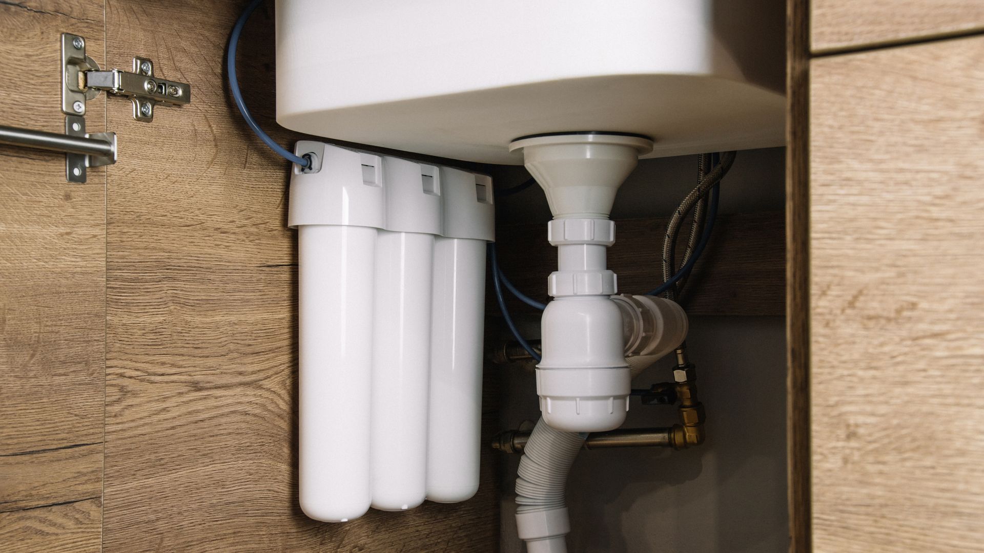 Water filter system installed under a sink. Three white cylindrical filters are connected to plumbing pipes.
