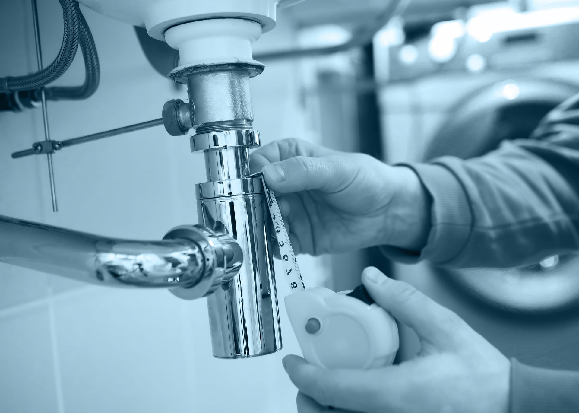 Hands working on a chrome sink drain under a sink, in a bathroom.