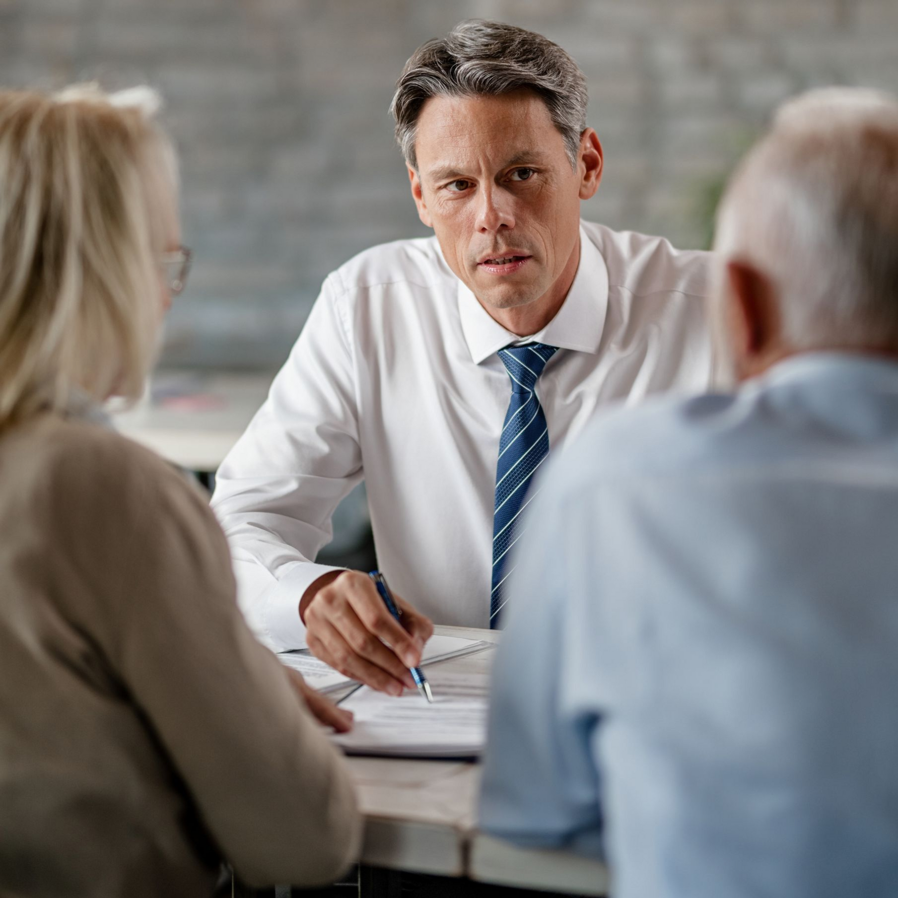 Business meeting with three people at a table, man in white shirt and blue tie listening intently