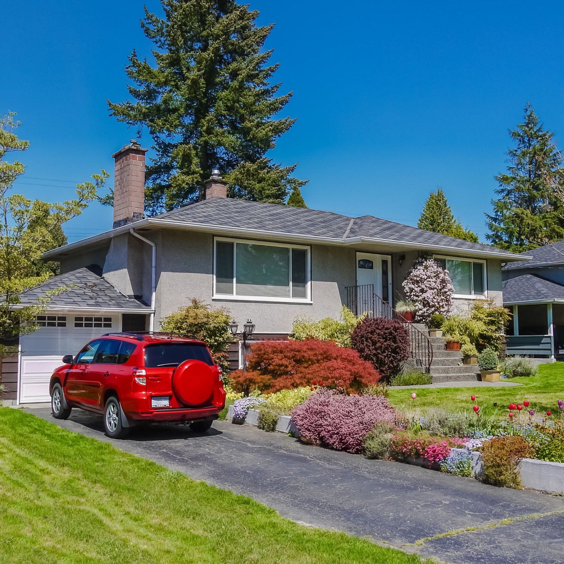 Suburban house with a red SUV in the driveway and a landscaped front yard