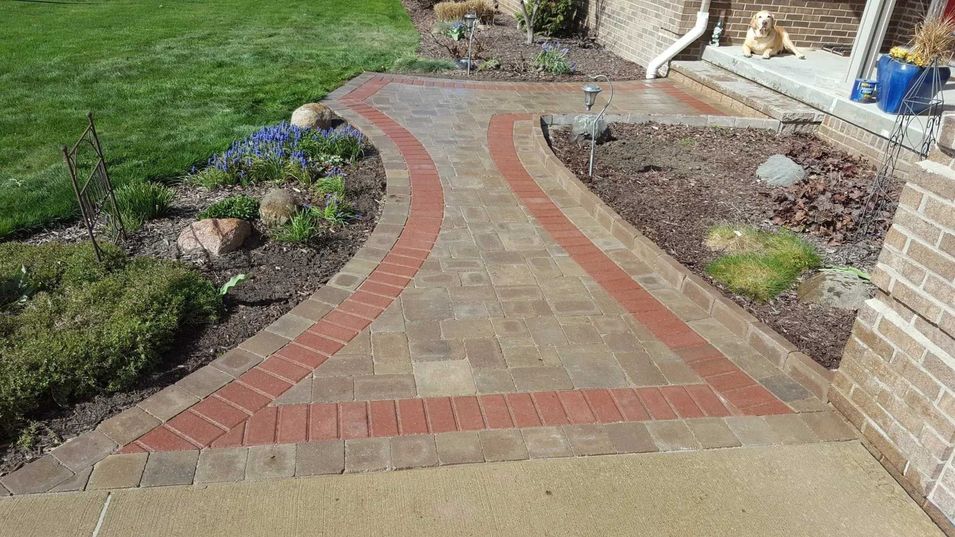 A brick walkway leading to a house with a dog on the porch.