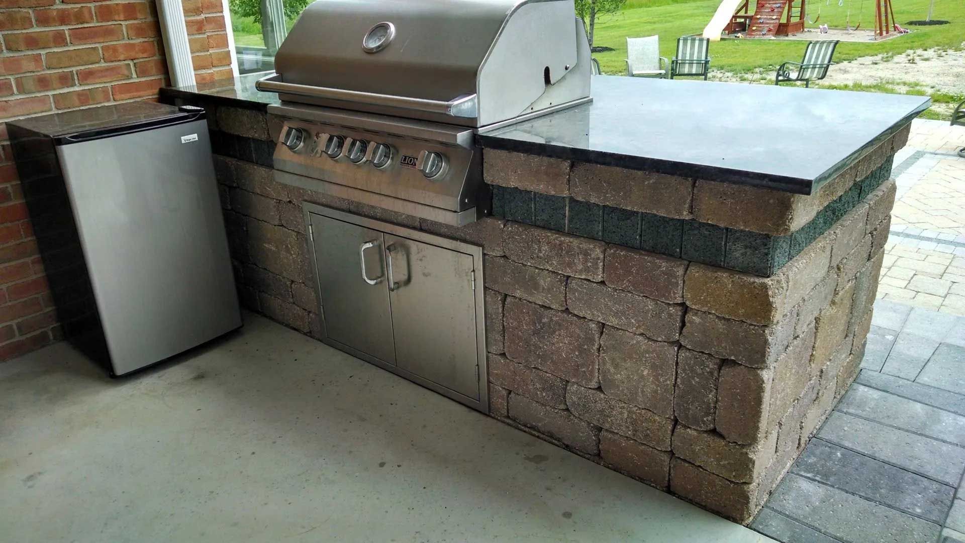 A grill is sitting on top of a brick counter next to a refrigerator.
