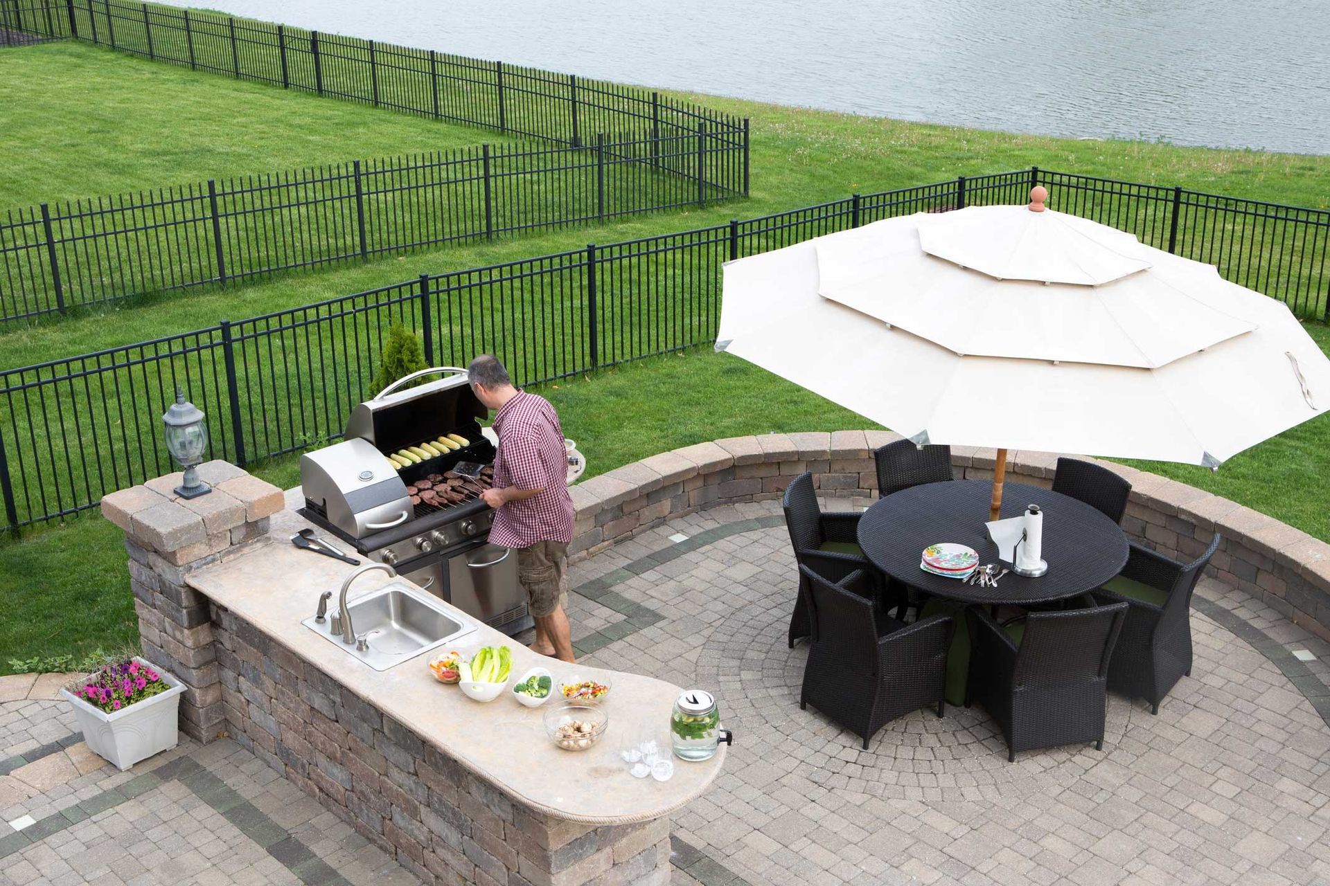 A man is cooking on a grill on a patio next to a table and chairs.