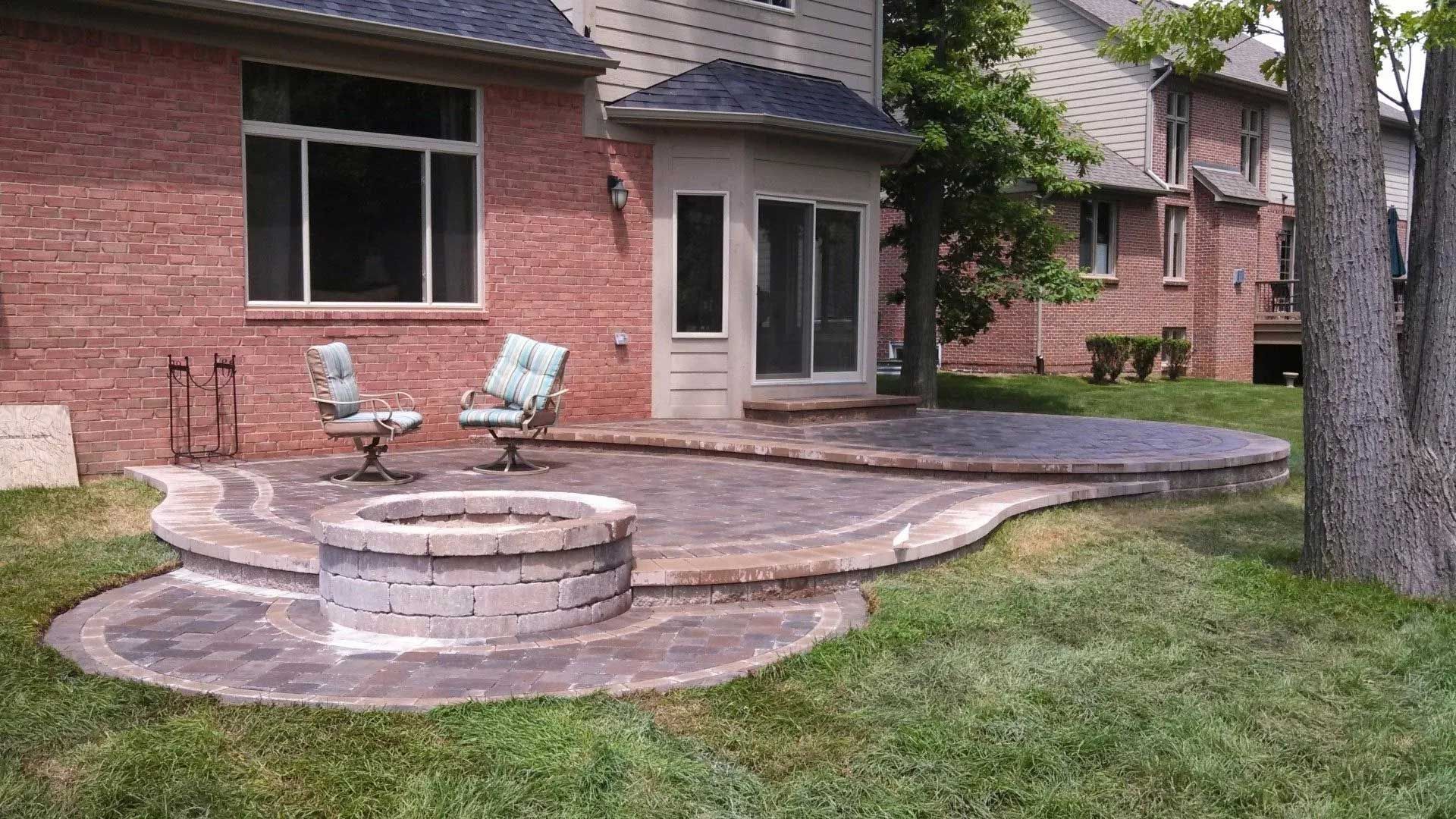 A patio with a fire pit and chairs in front of a brick house.