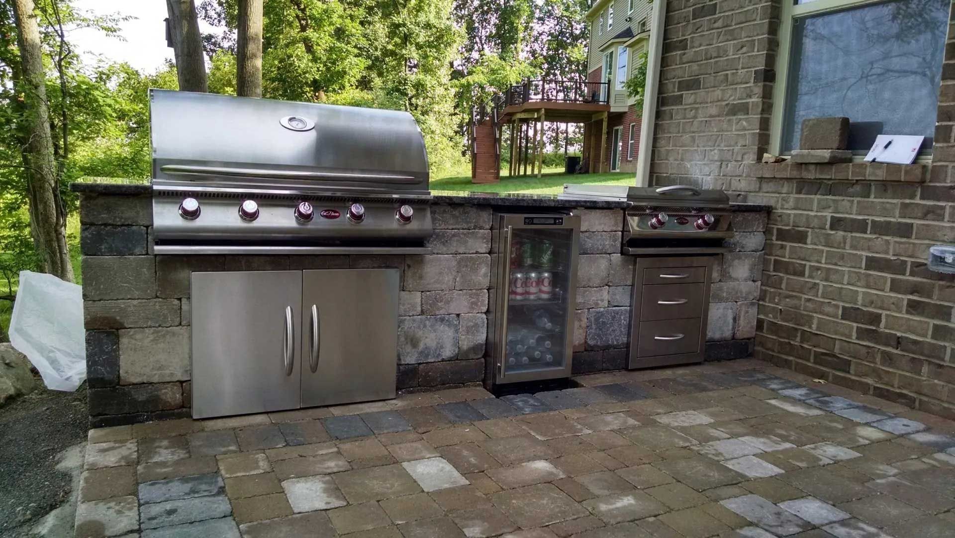 An outdoor kitchen with a grill and a refrigerator
