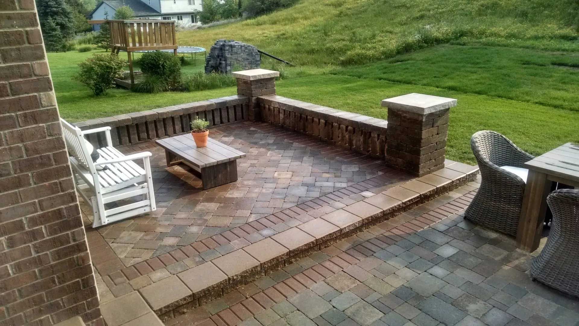 A brick patio with a table , chairs , and a bench.