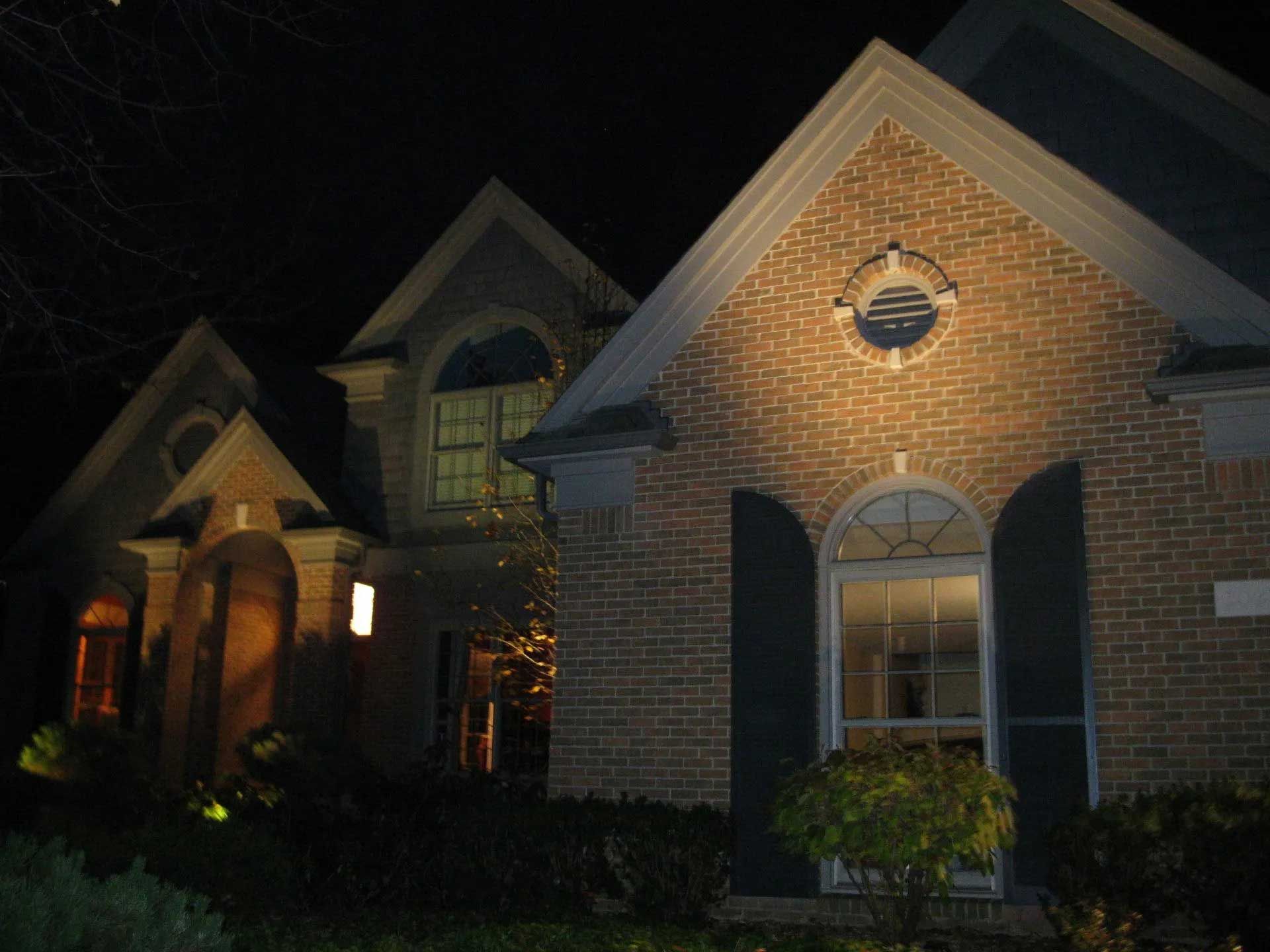 A brick house with black shutters is lit up at night