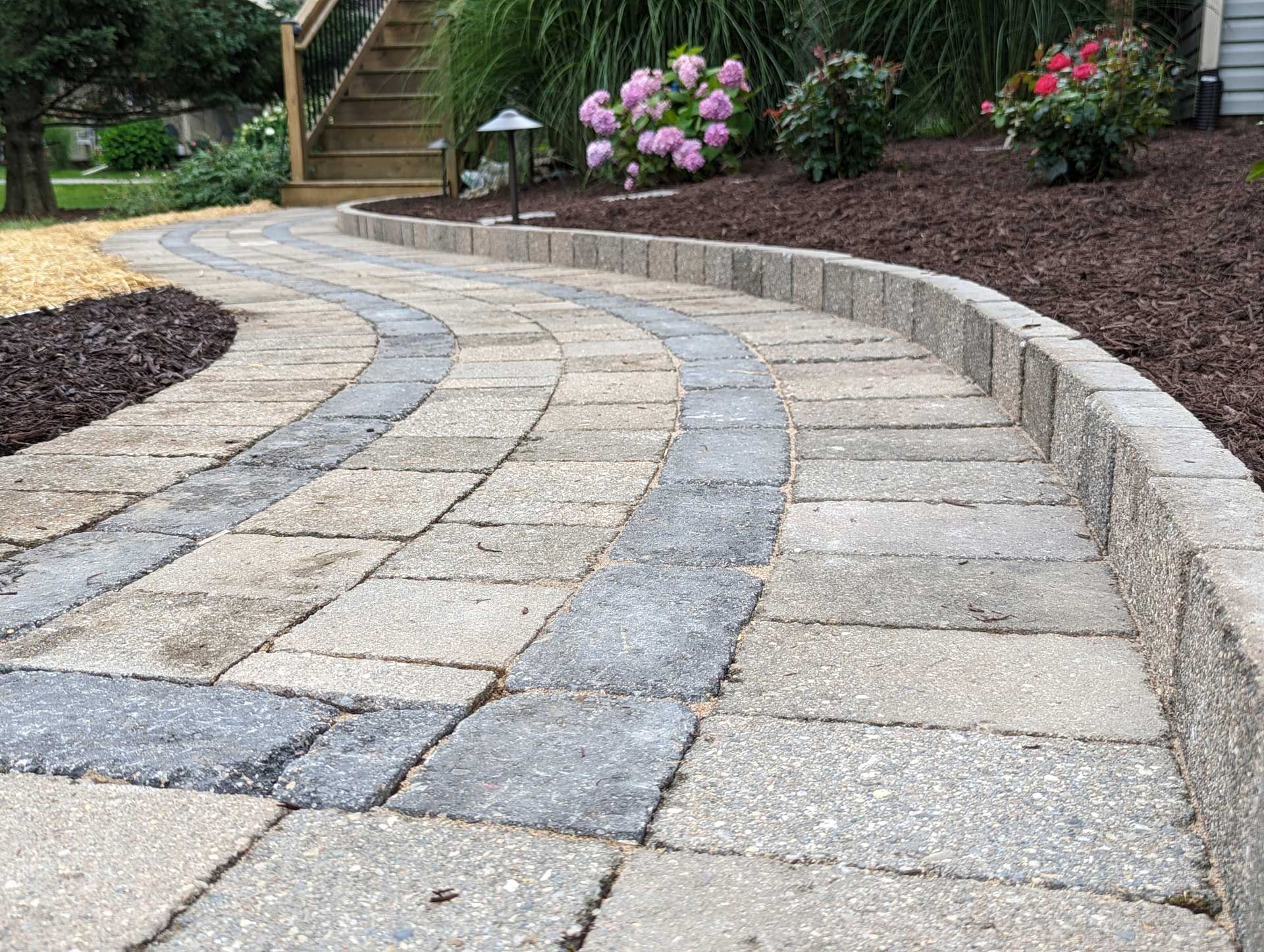 A brick walkway leading to a staircase in a garden.