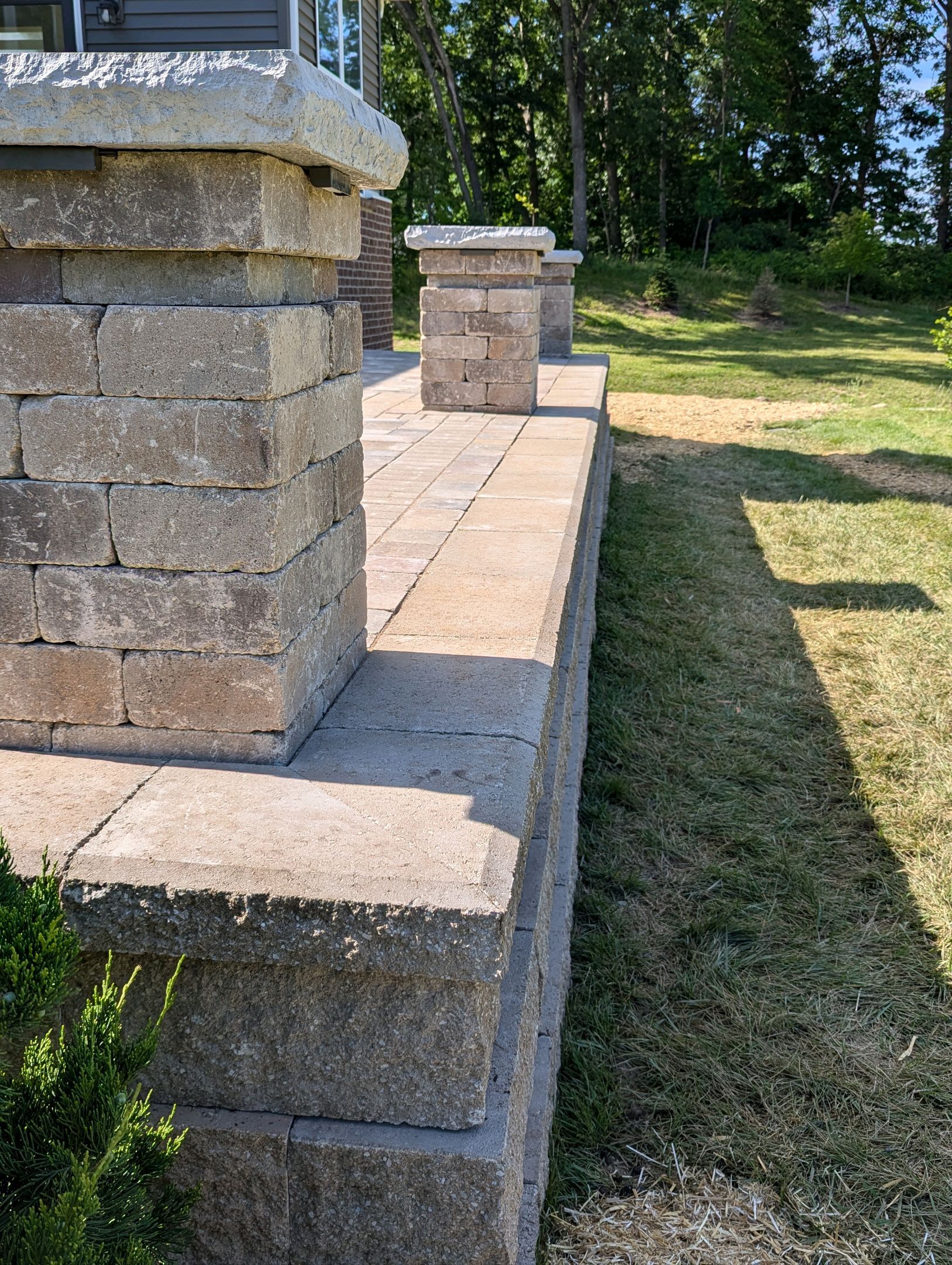 A stone wall surrounds a patio in a backyard.
