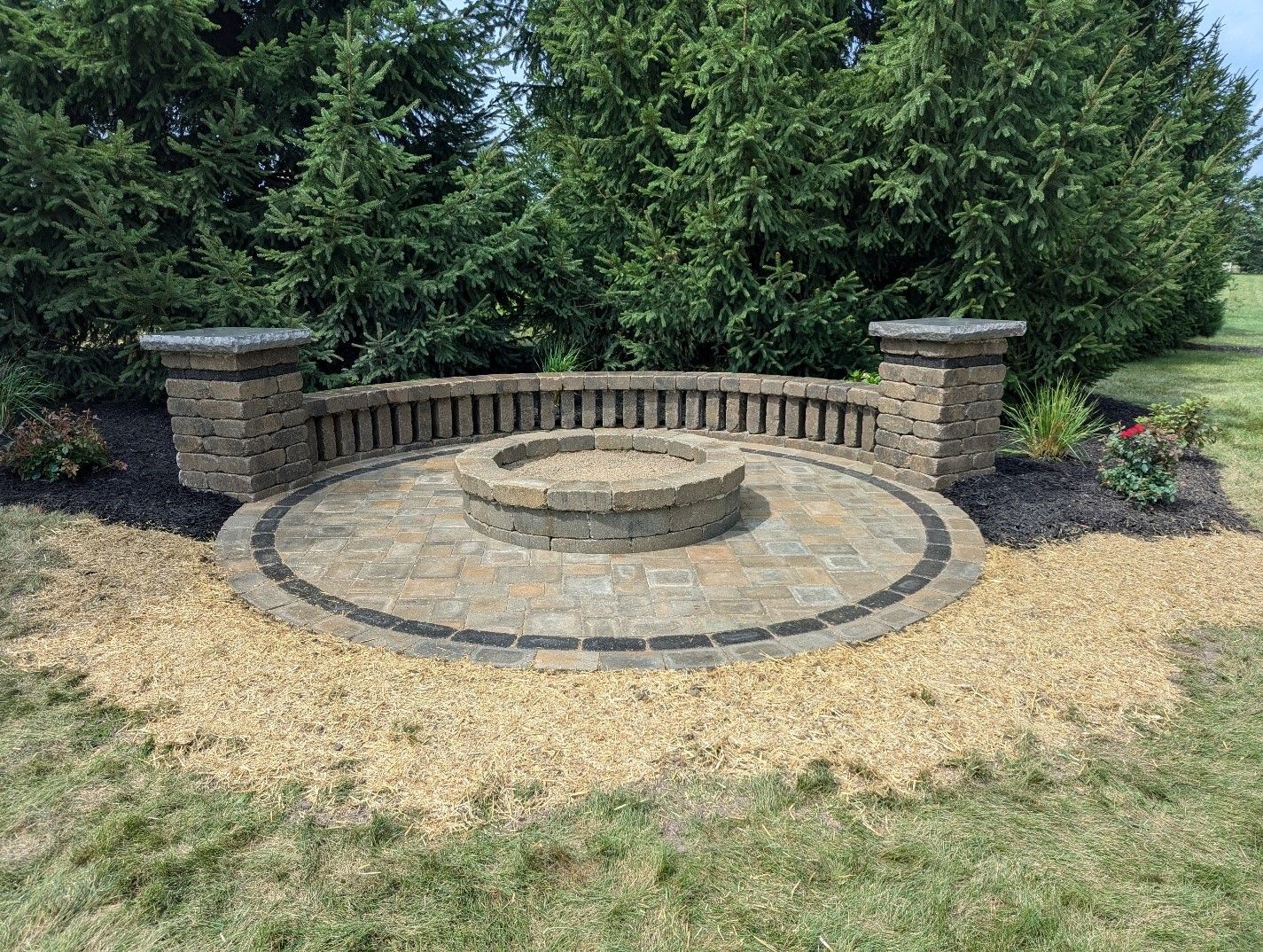 There is a fire pit in the middle of the yard surrounded by trees.