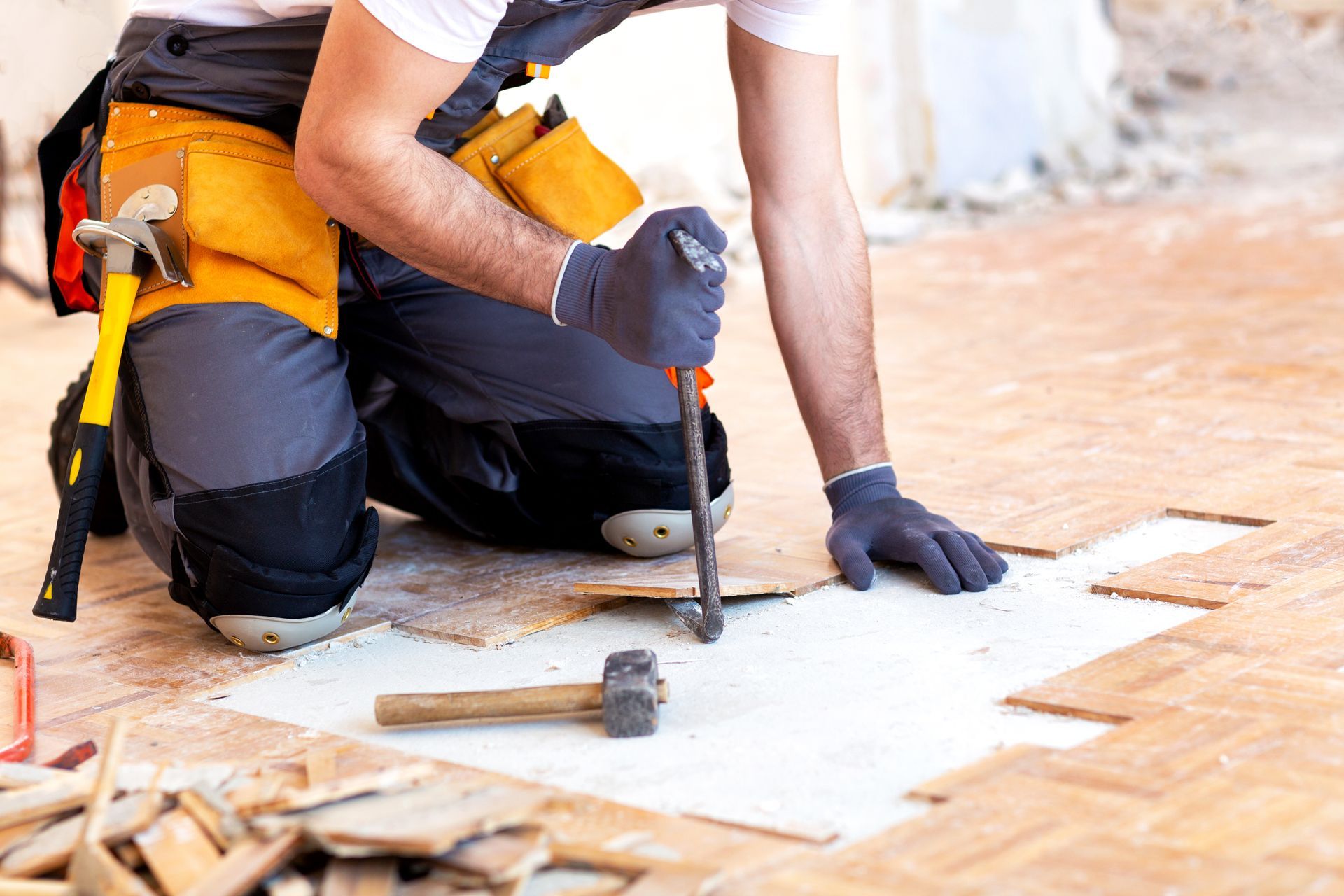 A construction worker in work clothes and gloves uses a pry bar to remove wooden floor tiles. A construction worker in work clothes and gloves uses a pry bar to remove wooden floor tiles.