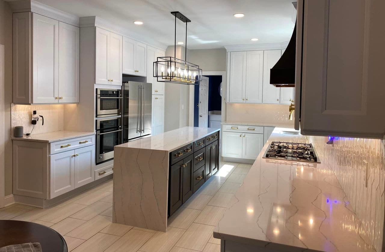 A kitchen with blue cabinets, a white-topped island with two stools, stainless steel appliances, and hardwood floors.