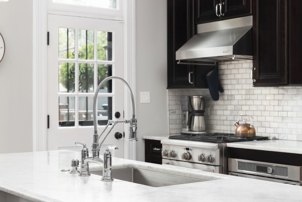 A kitchen island with a metal faucet in the foreground, facing a stove, subway tile backsplash, and a white paneled door.