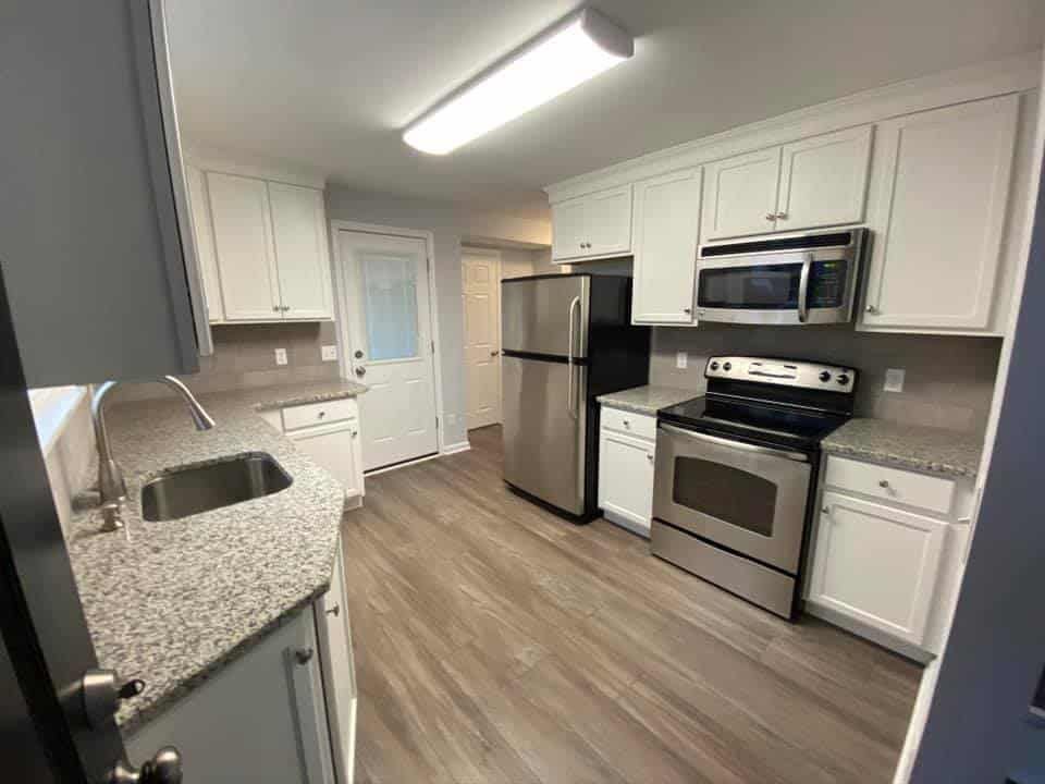 A modern kitchen with white cabinets, granite countertops, stainless steel appliances, and wood-look flooring.