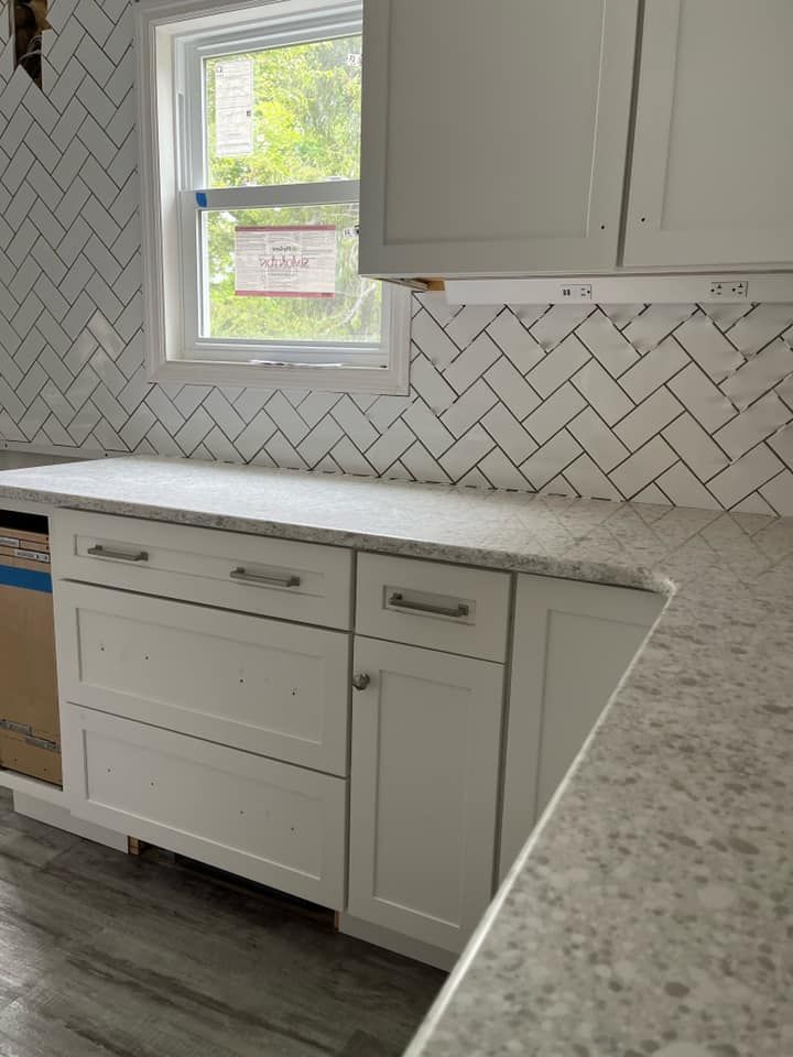Bright kitchen with white cabinets, herringbone tile backsplash, and a window above the countertop. Bright kitchen with white cabinets, herringbone tile backsplash, and a window above the countertop.