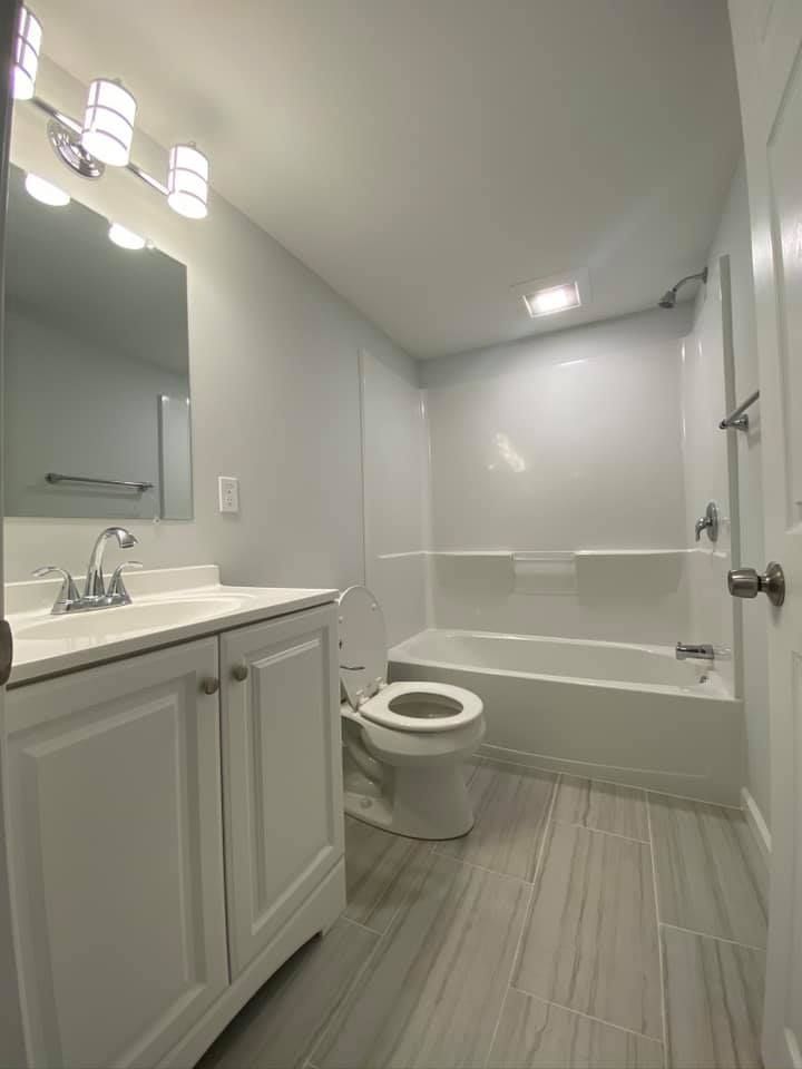 Modern bathroom featuring a white vanity with a silver faucet, a toilet, and a bathtub with a shower head.