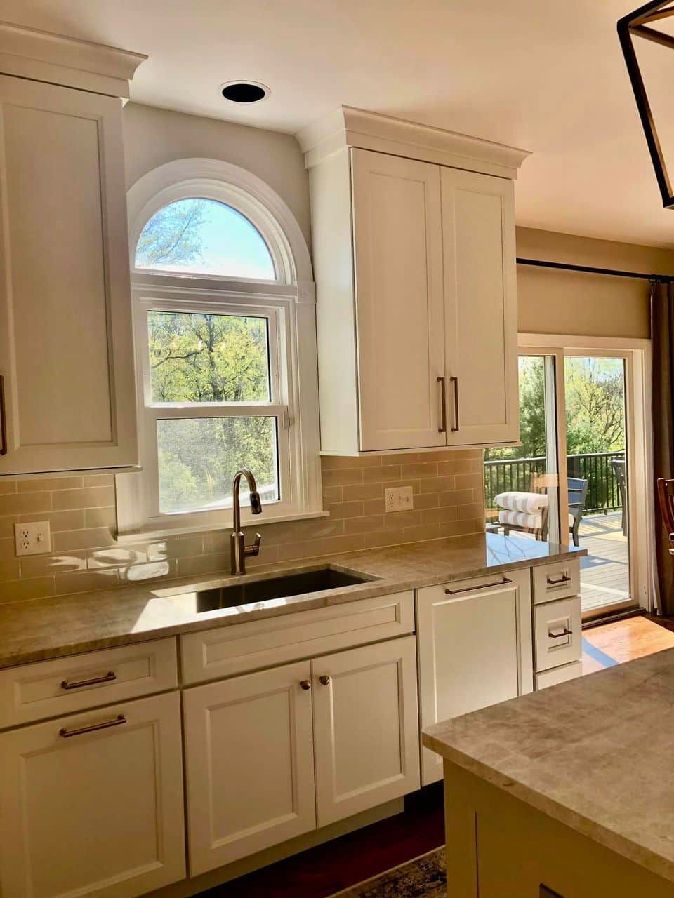 A kitchen interior with white cabinetry, a sink under an arched window, and a light countertop island in the foreground.