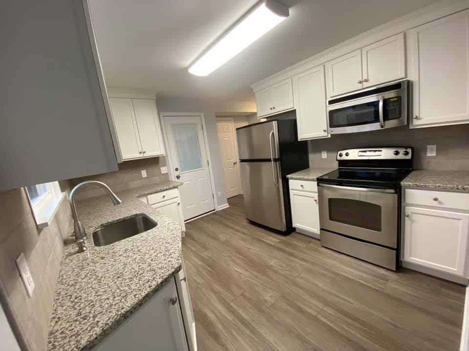 A bright kitchen featuring white cabinets, stainless steel appliances, granite countertops, and light wood-look flooring.