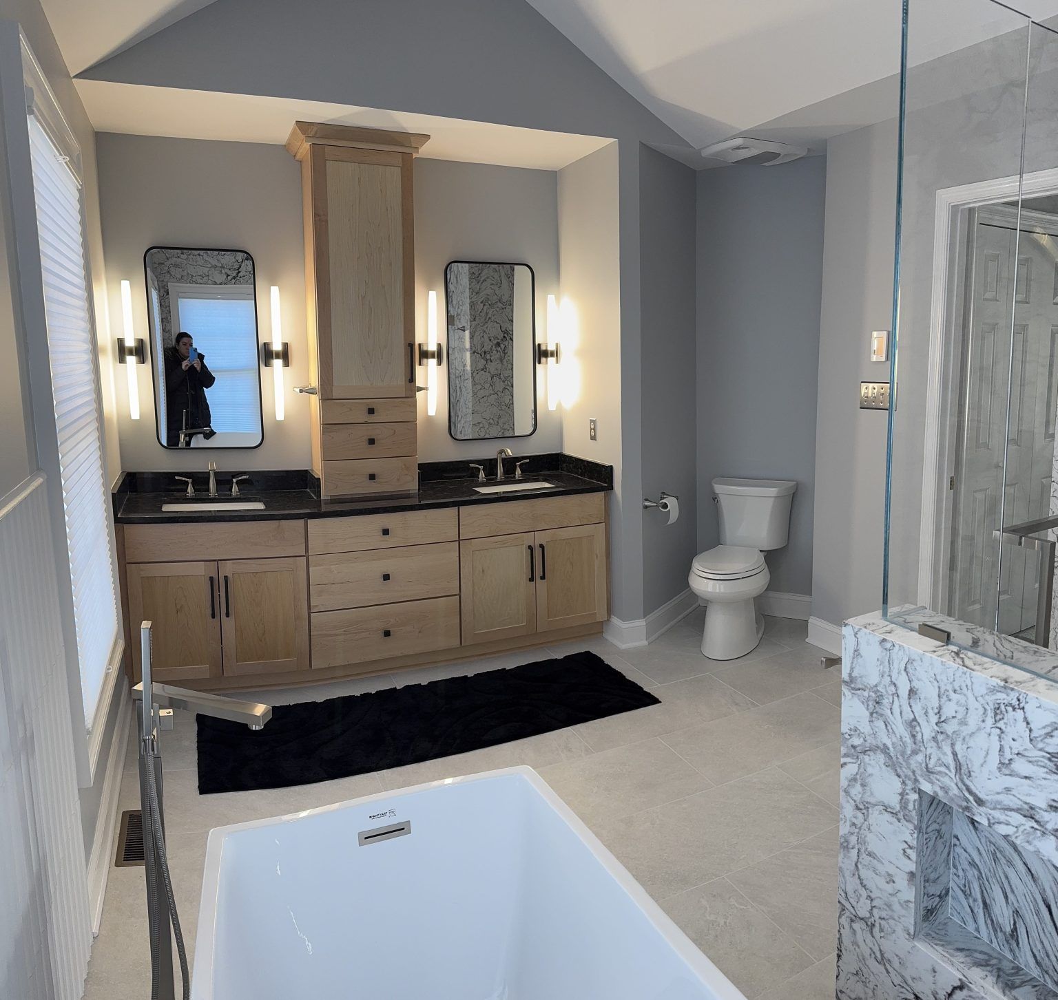 A modern bathroom with light wood dual vanities, white marble features, a freestanding tub, and a toilet. A modern bathroom with light wood dual vanities, white marble features, a freestanding tub, and a toilet.