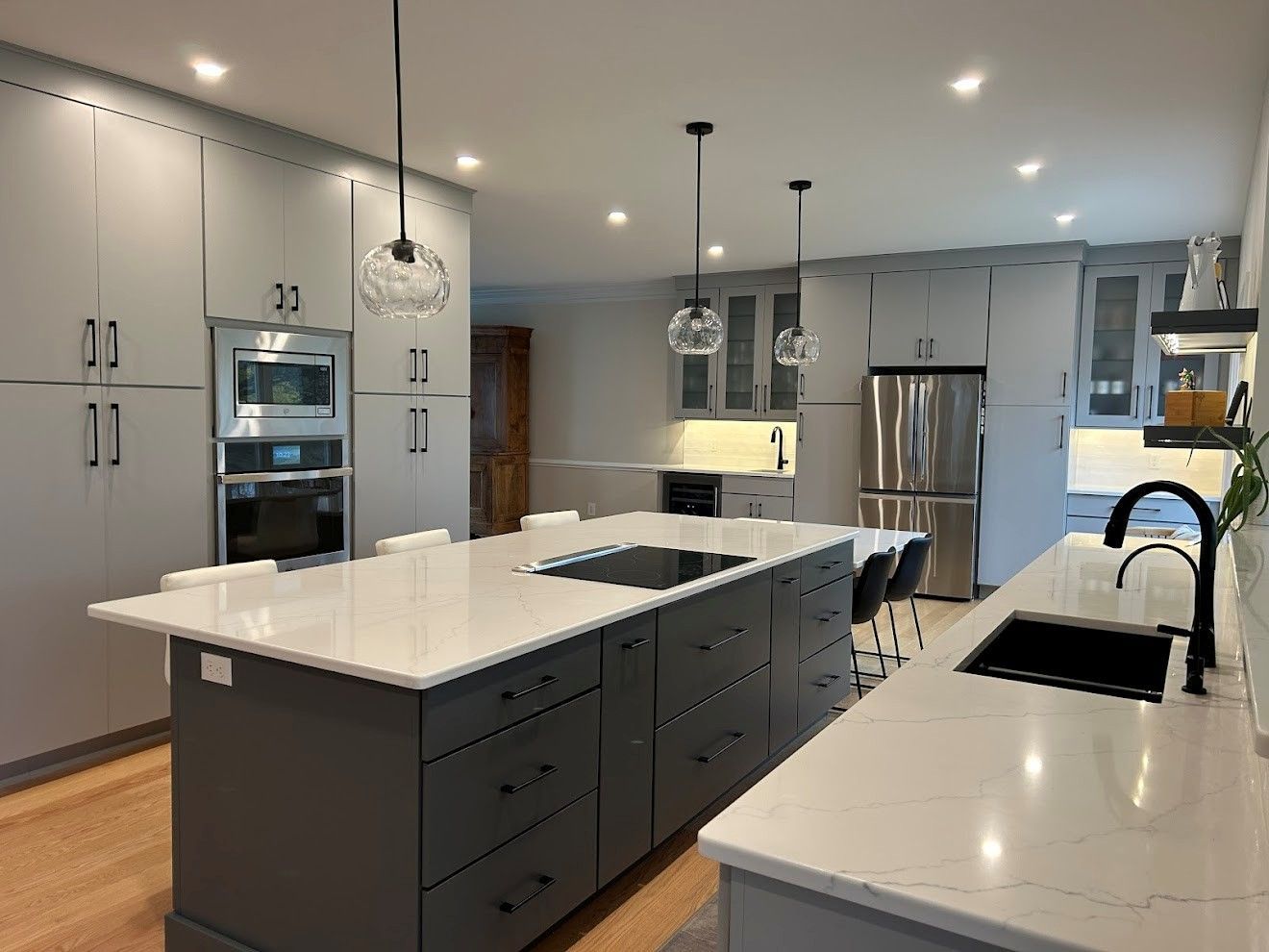 A brightly lit kitchen with white cabainets, a speckled countertop, a large kitchen island, and a herringbone-tiled wall.