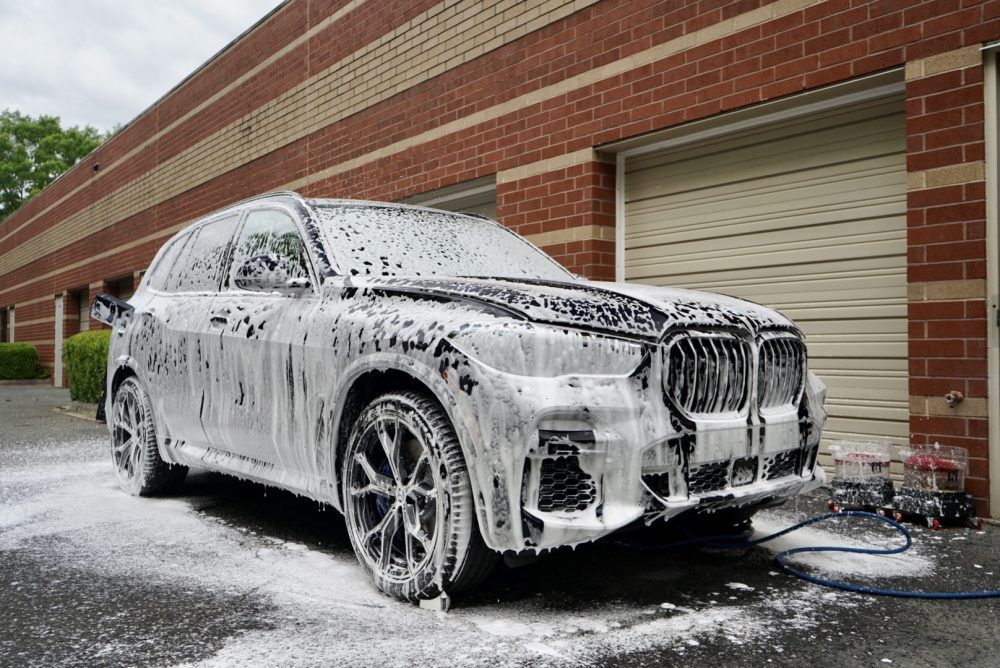 A car is covered in foam in front of a brick building.