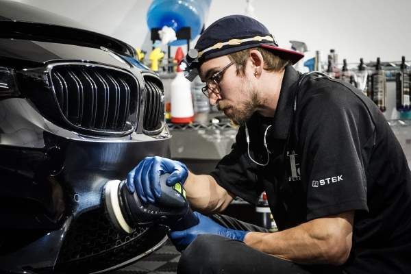 A man is polishing the front of a car in a garage.