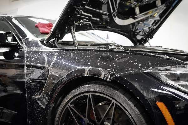 A black car with the hood open is covered in protective film.