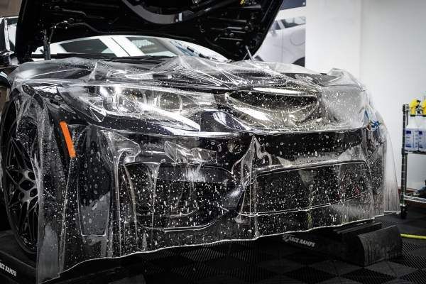 A black car is covered in plastic wrap in a garage.