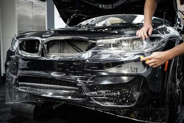 A man is applying protective film to the front of a black car.