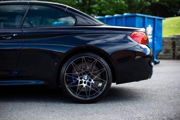 A black bmw m4 is parked in a parking lot next to a blue dumpster.