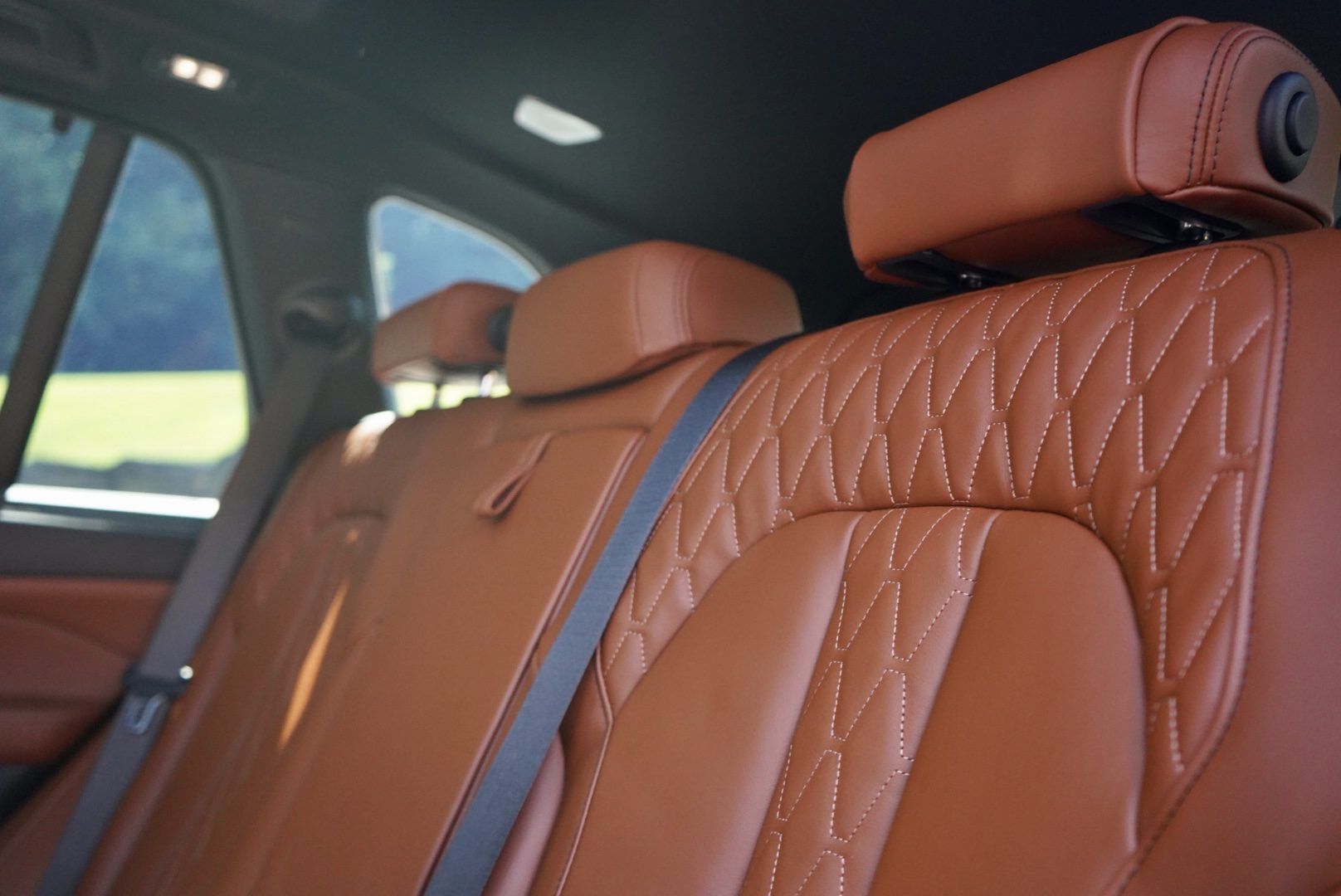 The back seat of a car with brown leather seats and black seat belts.