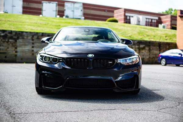 A black bmw m4 is parked in a parking lot in front of a building.