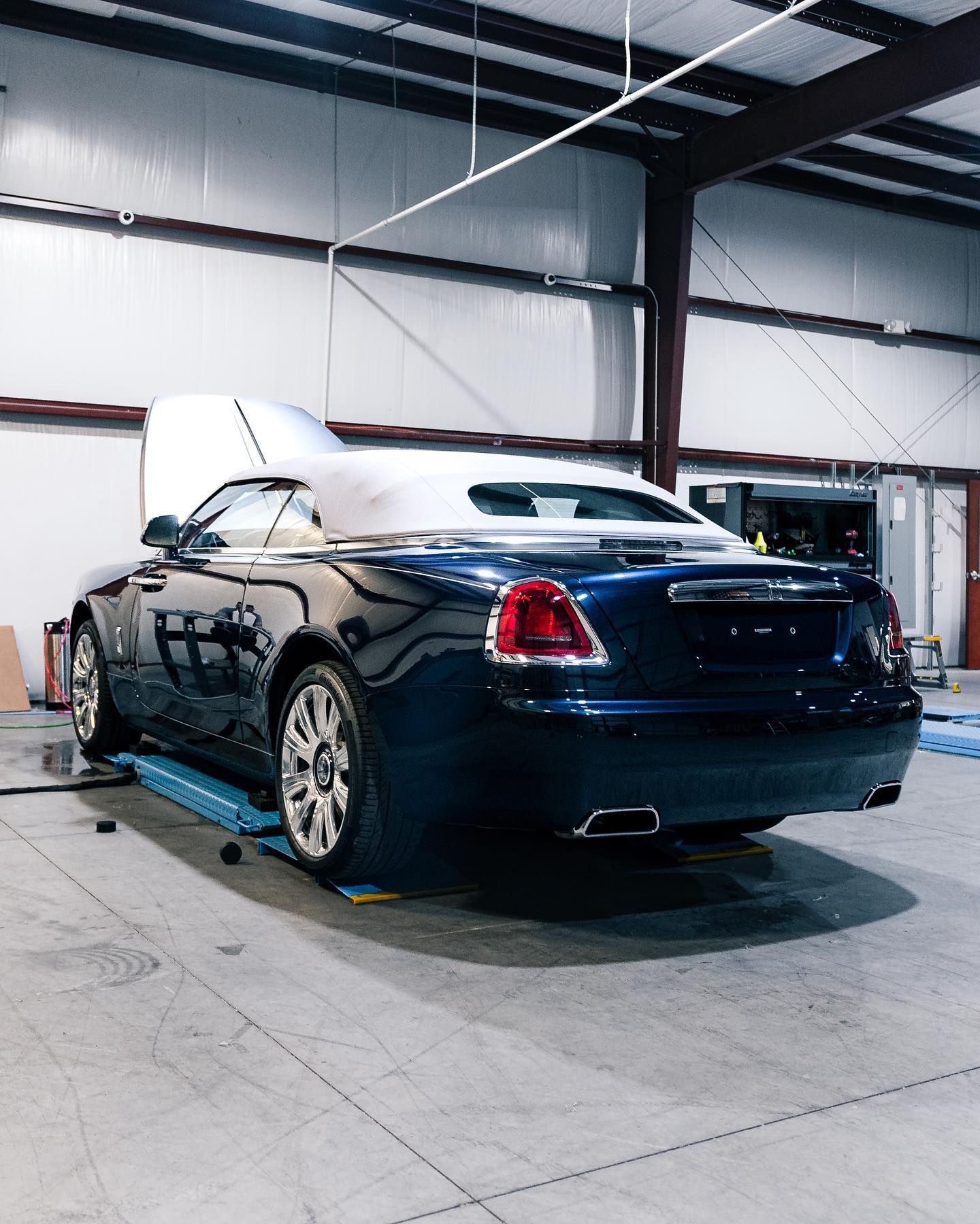A blue car with the hood up is parked in a garage.