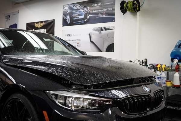 A black bmw is parked in a garage with the hood up.