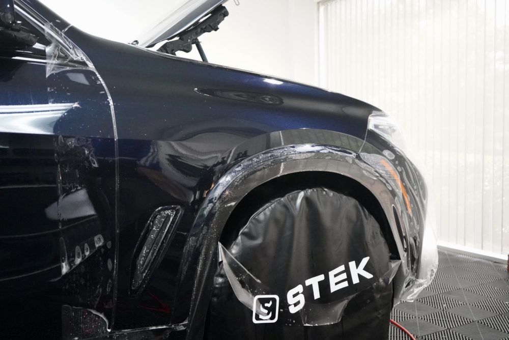 The fender of a black car is wrapped in plastic.
