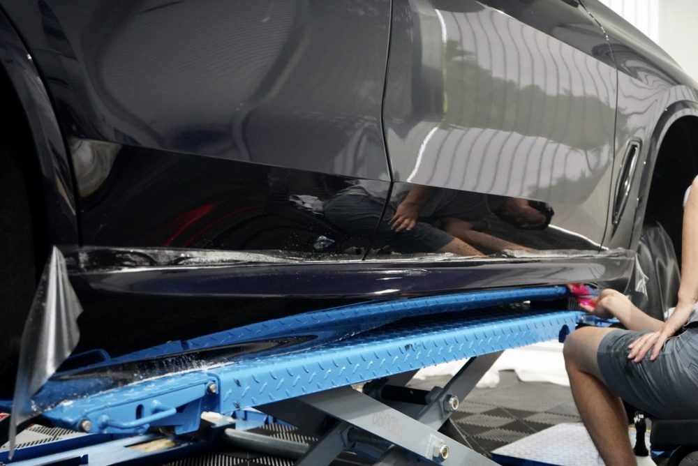 A woman is sitting in front of a car on a lift.