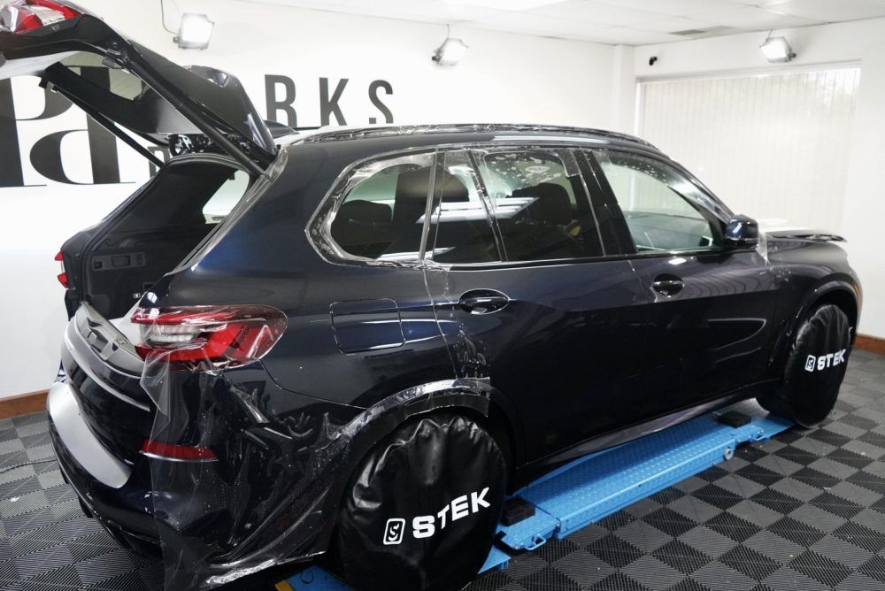 A black car is parked in a garage with the trunk open.