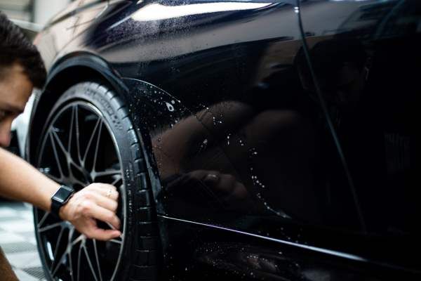 A man is cleaning the wheel of a black car.