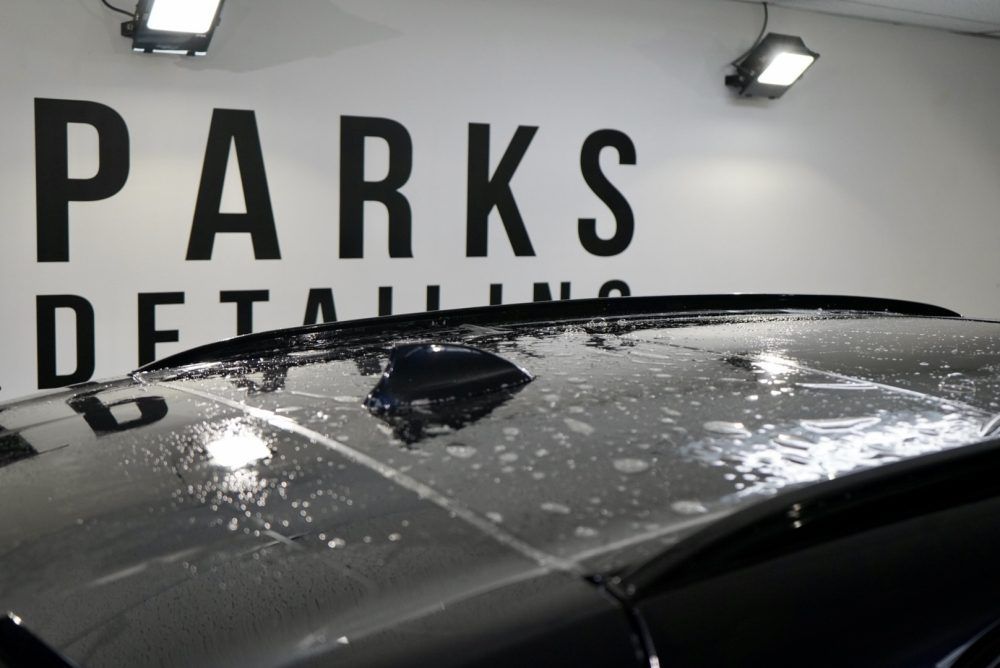 A car is sitting in front of a wall that says parks detailing