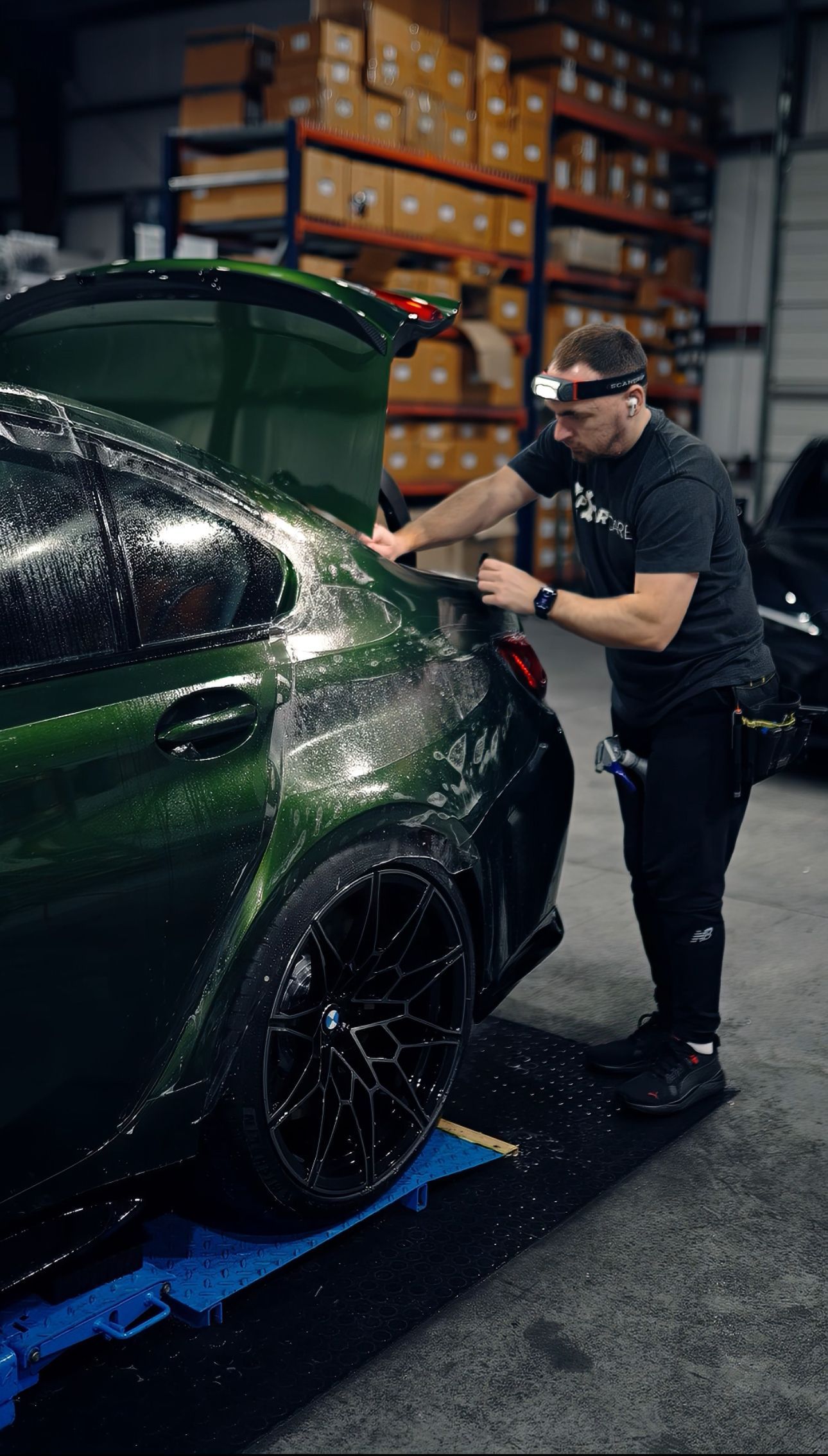 A man is standing next to a green car in a garage.
