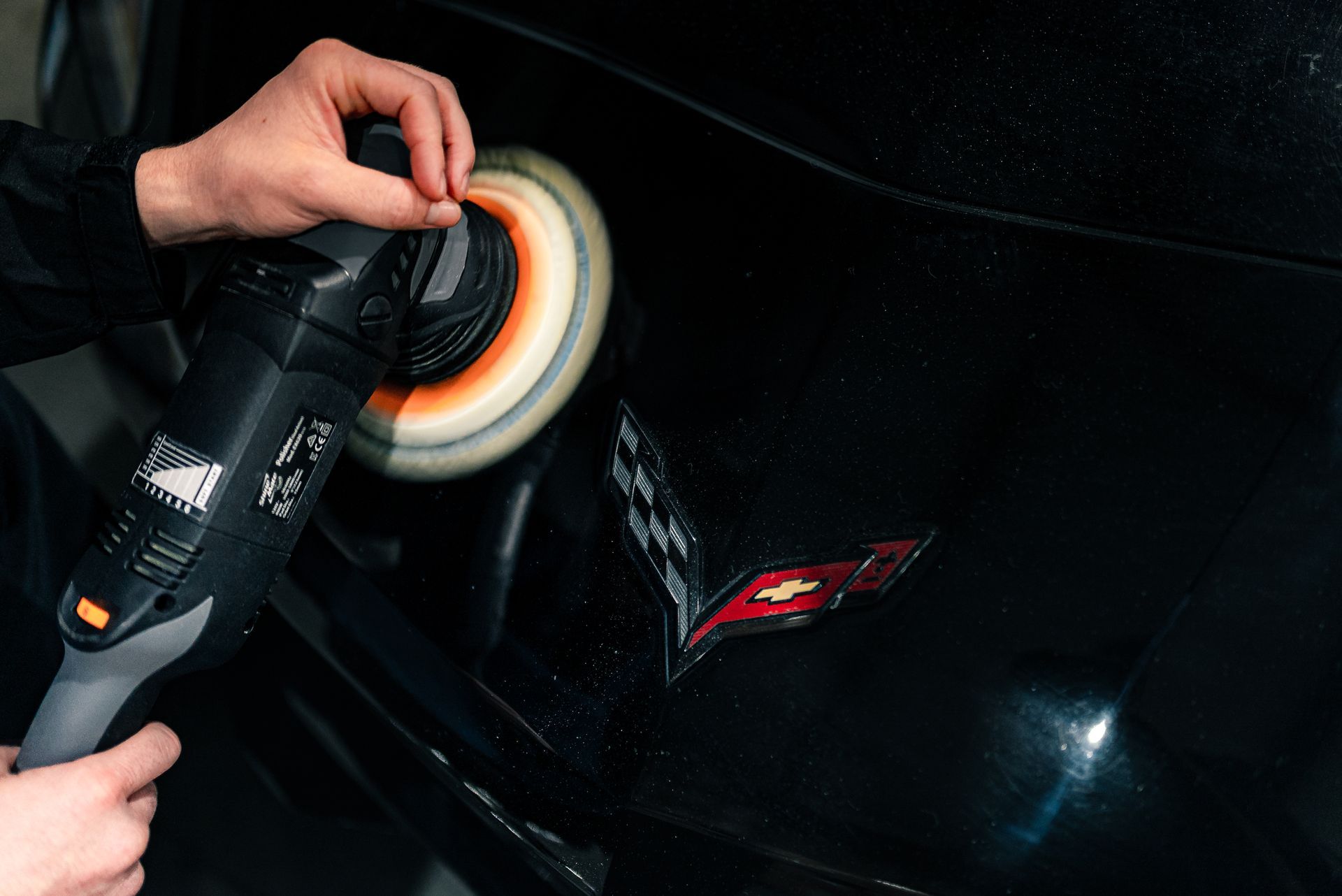 A person is polishing a black car with a machine.